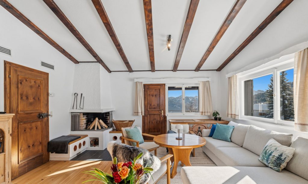 Das Bild zeigt das lichtdurchflutete Wohnzimmer des Ferienhaus Eixer am Bödele. Es ist mit einem offenen Kamin, einer gemütlichen Couch und einem Tisch ausgestattet.