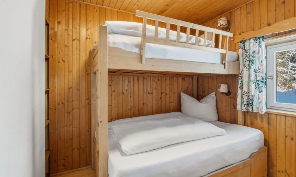 Das Bild zeigt ein Schlafzimmer des Ferienhaus Eixer am Bödele. Das Schlafzimmer ist mit einem Stockbett und einem Regal ausgestattet.